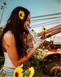 A young woman smoking from a bong with a sunflower in her hair