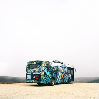 a bus covered in cool art driving across a desert we've dubbed the cannibus